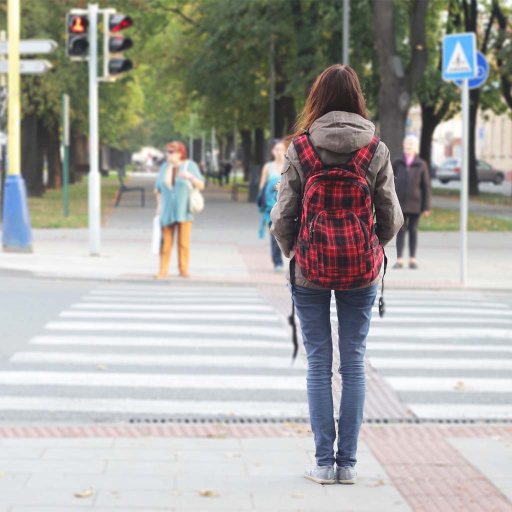 Female teen with plaid backpack using cross walk